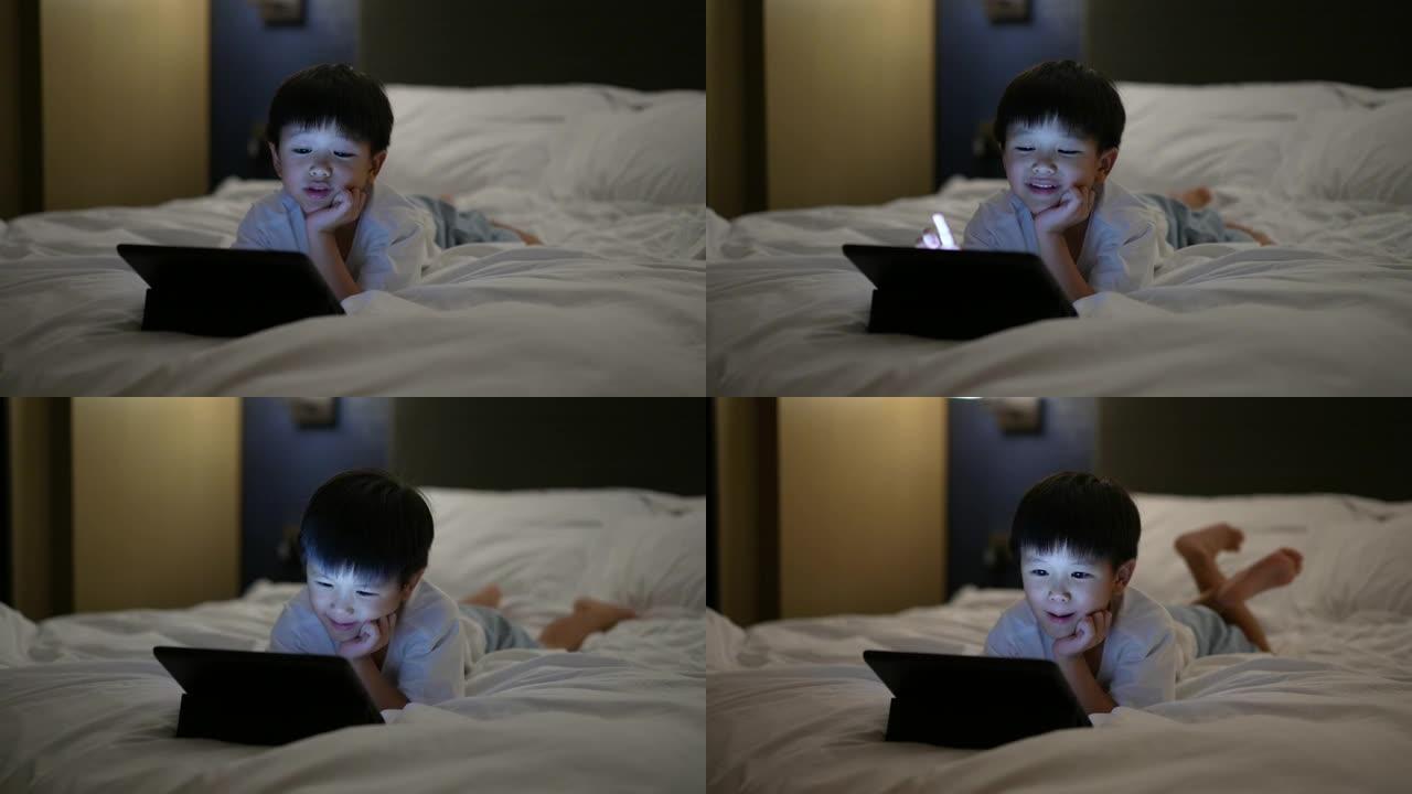 亚洲孩子在床上使用数字平板电脑。家庭时间的概念