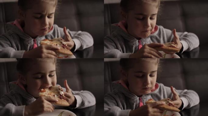 孩子吃披萨。饥饿的小女孩坐在厨房的餐桌上，从盘子里吃美味的意大利披萨。不健康的营养快餐。孩子吃午饭的