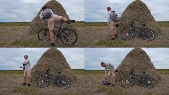 一个骑自行车的人在田野的干草堆附近停下来休息一下。他从自行车上爬下来，将其靠在干草堆上，然后脱下背包