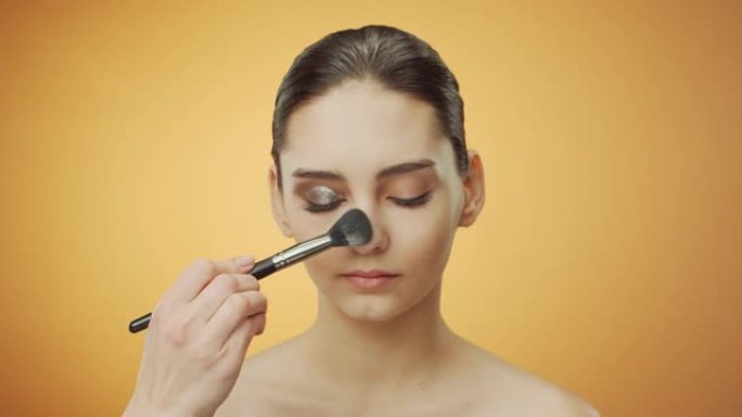 化妆申请的步骤。化妆师使用化妆刷在黑发模特的眼睛下方撒粉。
