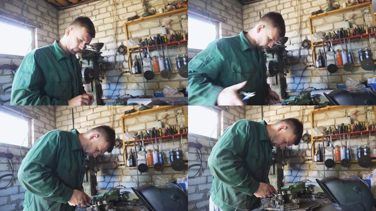 在车间使用工具进行统一维修车辆细节的男机械师。工作服专业修理工在他的车库工作。维护服务的概念。起重机