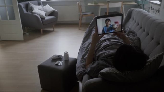 生病的男性成年人躺在沙发上，与护士进行视频聊天