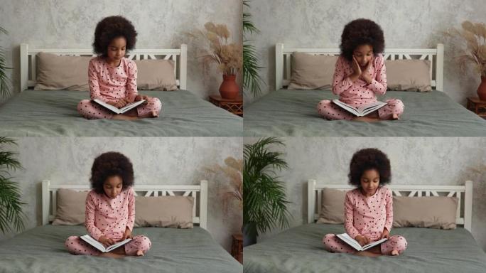 可爱的小非洲裔美国女孩读童话书，脸上带着哇惊讶和热情的表情。穿着睡衣的少女坐在卧室的床上。慢动作