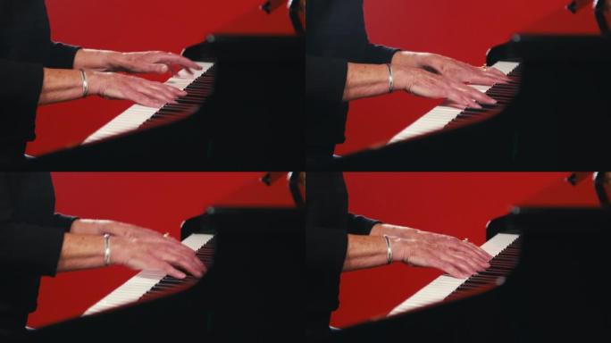 一个成年白人妇女的手在红色工作室背景前弹钢琴的特写镜头