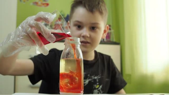 这个男孩在家进行化学实验。将带有染料的液体添加到油瓶中。一位年轻的化学家