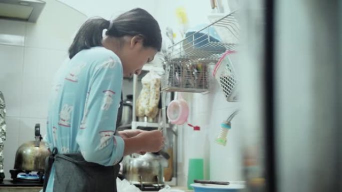 亚洲女孩穿着围裙脱皮，在厨房里为烹饪前准备食物去皮虾，生活方式理念。