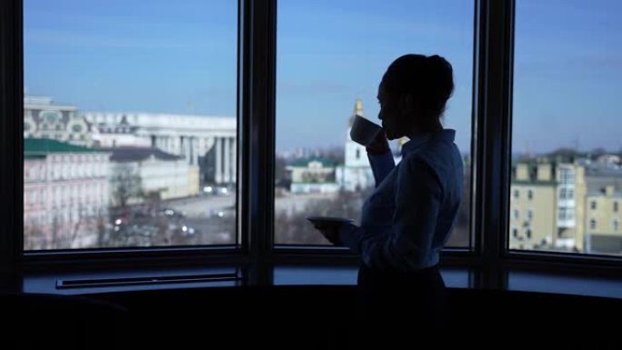 自信的女人在酒店的窗户旁喝茶