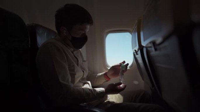 戴口罩的人消毒手在飞机上使用酒精消毒剂。新型冠状病毒肺炎期间的新常态、安全和旅行。在冠状病毒流行期间