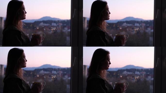 女人站在窗边，端着一杯茶，看着日落。