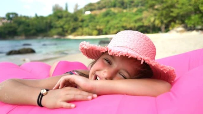 一个戴着粉红色草帽的小女孩躺在海滩上的充气沙发上。冠状病毒出口