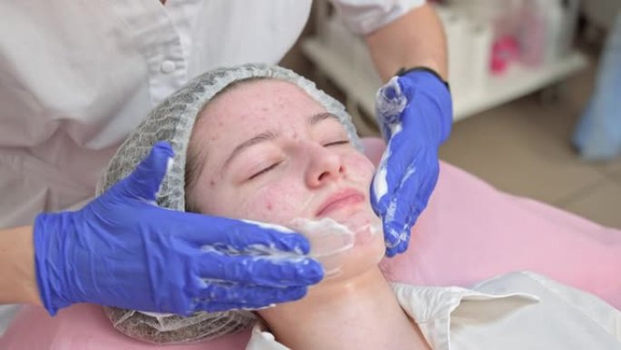 美容师双手戴着蓝色手套触摸白人少女病人的脸，在美容院做清洁脱皮程序。痤疮，皮肤治疗，问题皮肤。护肤概