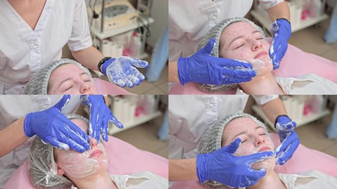 美容师双手戴着蓝色手套触摸白人少女病人的脸，在美容院做清洁脱皮程序。痤疮，皮肤治疗，问题皮肤。护肤概