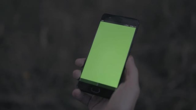 一个男人手持绿色屏幕的智能手机的特写镜头。股票。模糊背景上色度键的现代手机