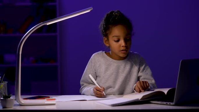 女孩把课本上的任务改写成笔记本。一名女学生在夜灯的灯光下坐在桌子旁。作业，远程学习。特写。慢动作就绪