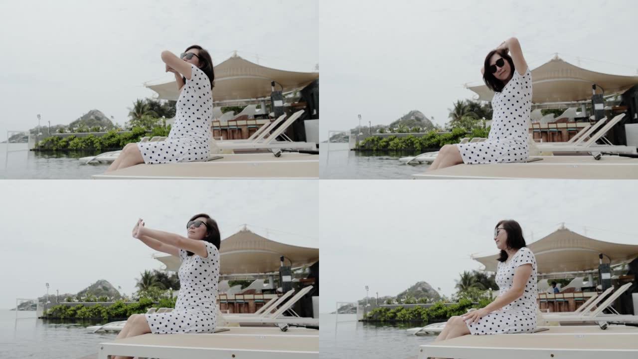 快乐的亚洲女人在度假期间在酒店的日光浴床上举手放松，生活方式理念。