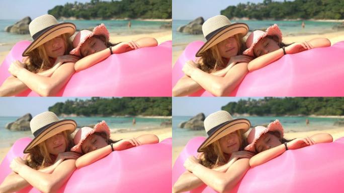 戴着草帽的妈妈和女儿在躺在粉红色充气沙发上的海滩上享受闲散