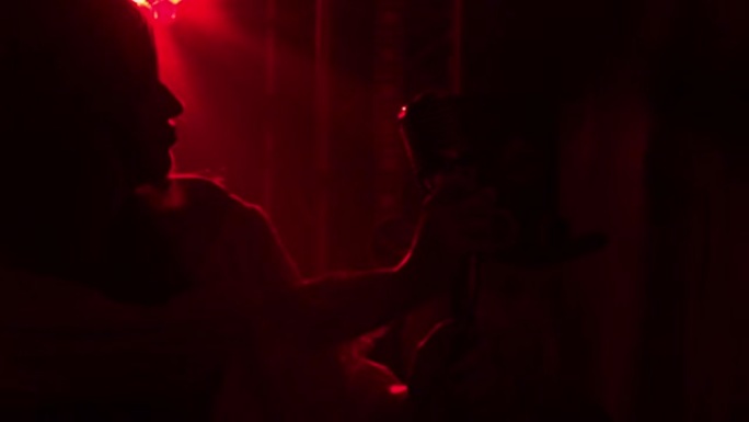 摇滚乐队的女歌手在黑烟酒吧里的红光表演。一个穿着复古衣服的女人和一个戴着帽子的男人随着音乐的节奏移动