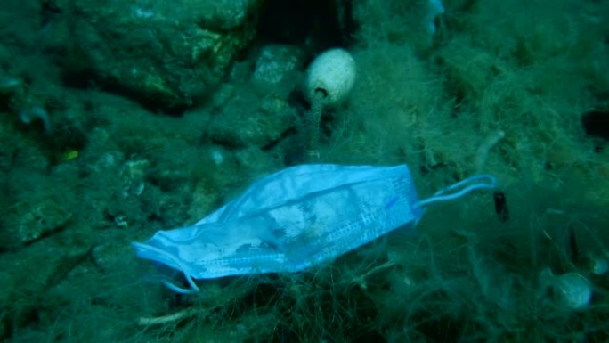 用过的口罩躺在丢失的渔网上。冠状病毒新型冠状病毒肺炎正在造成污染，因为废弃的二手口罩会污染海洋和塑料