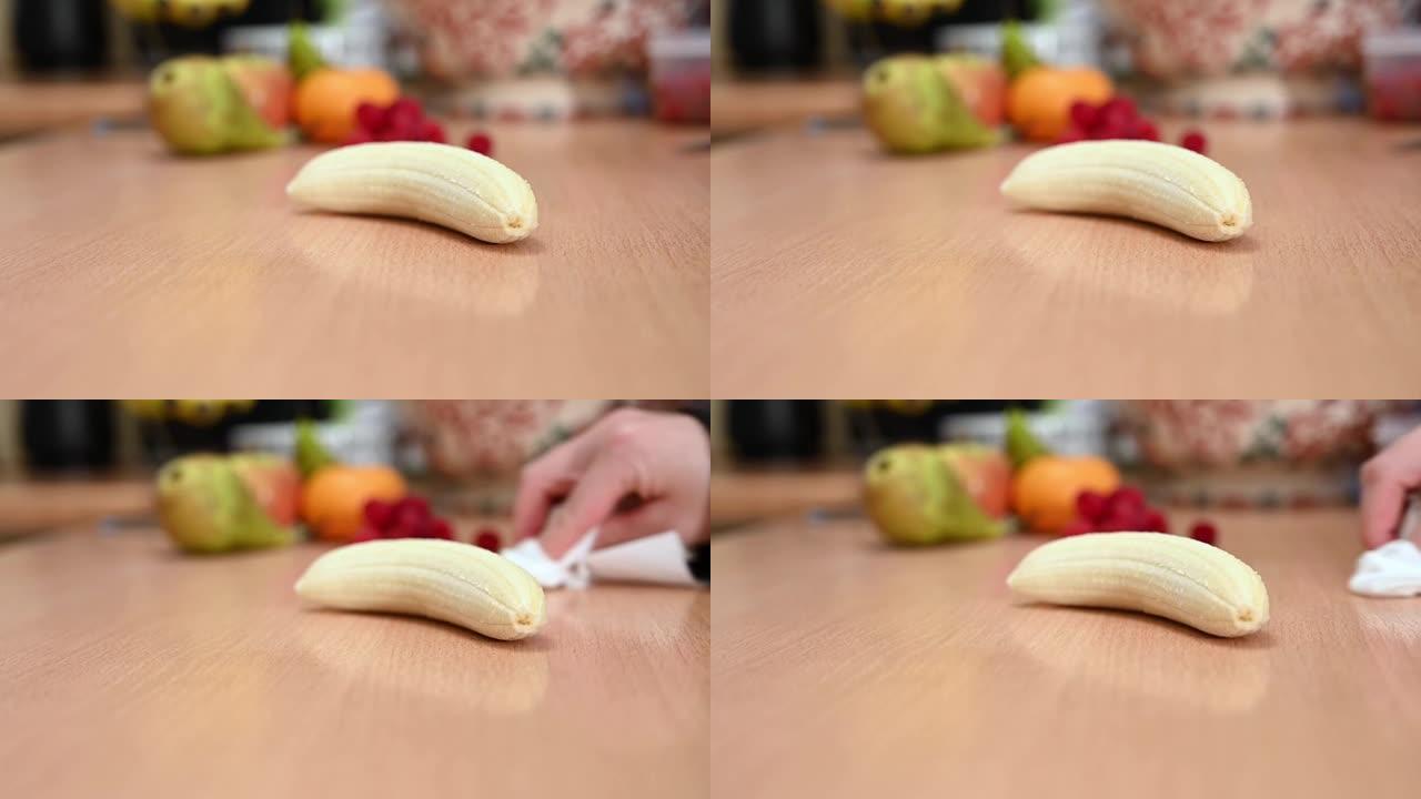 一只手在去皮的香蕉周围擦拭厨房台面的慢动作镜头。背景中的焦点水果