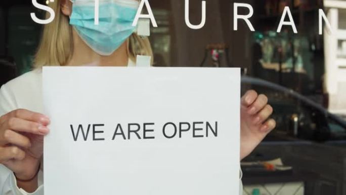 咖啡馆或餐馆和企业在冠状病毒检疫结束后重新开放。戴着口罩的女人在门店转动招牌。covid封锁后的小企