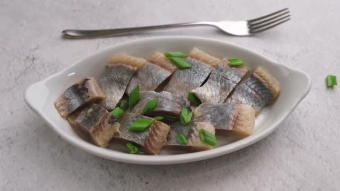 白盘上的鲱鱼片撒上大葱。咸海鱼，传统的冷小吃。