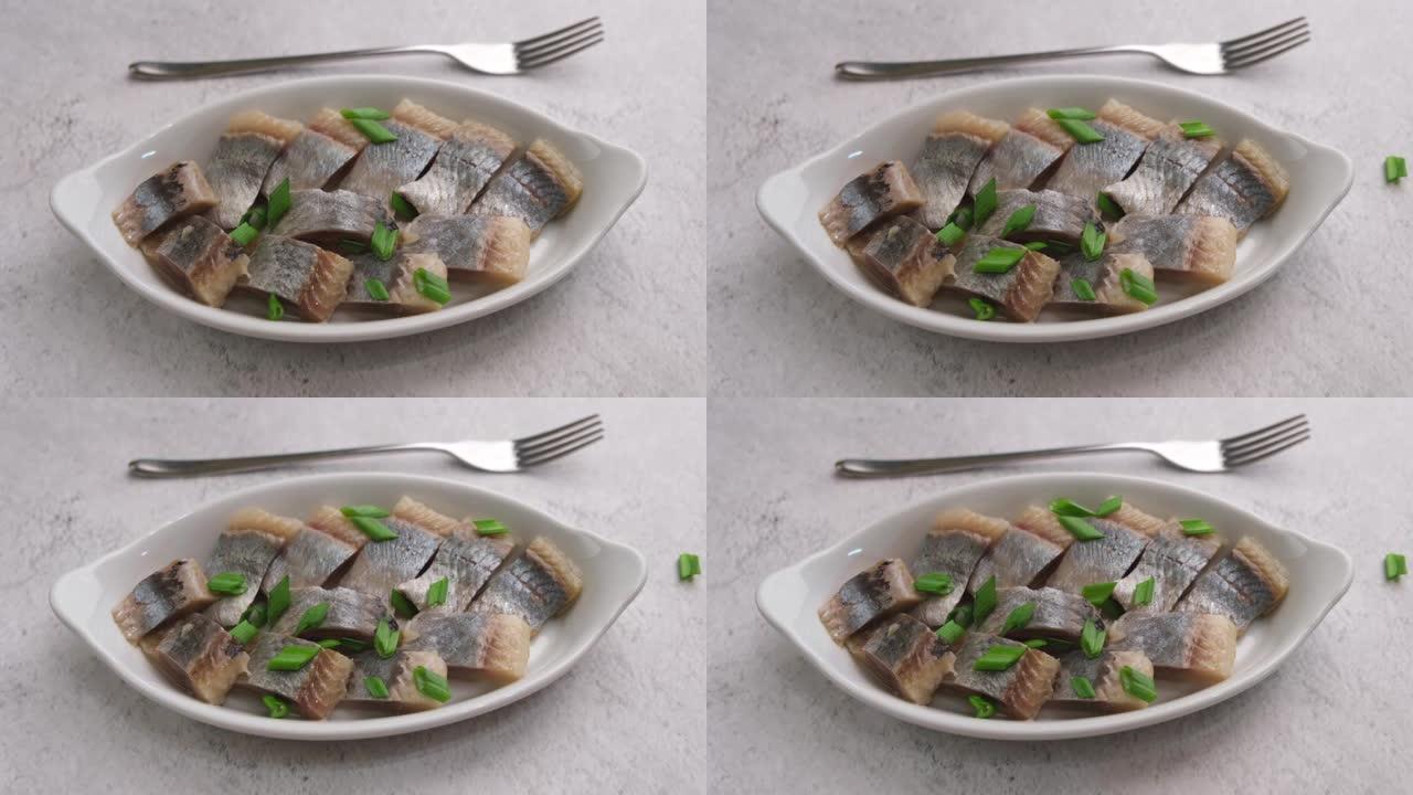 白盘上的鲱鱼片撒上大葱。咸海鱼，传统的冷小吃。