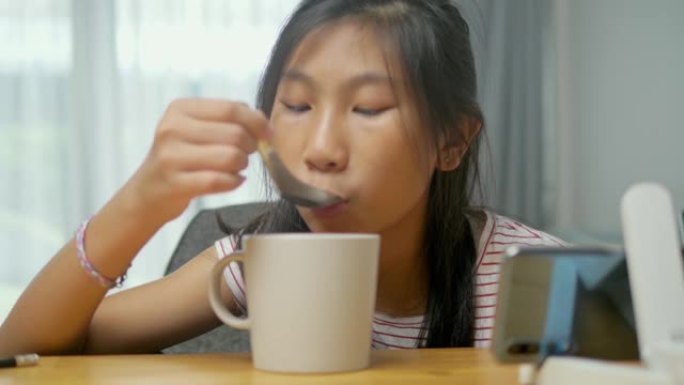 亚洲女孩在家里喝一杯热巧克力时看电影或病毒视频，生活方式概念。