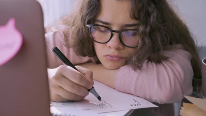 戴眼镜的悲伤女人在笔记本电脑躺在桌子上的纸上写字