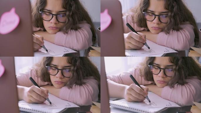 戴眼镜的悲伤女人在笔记本电脑躺在桌子上的纸上写字