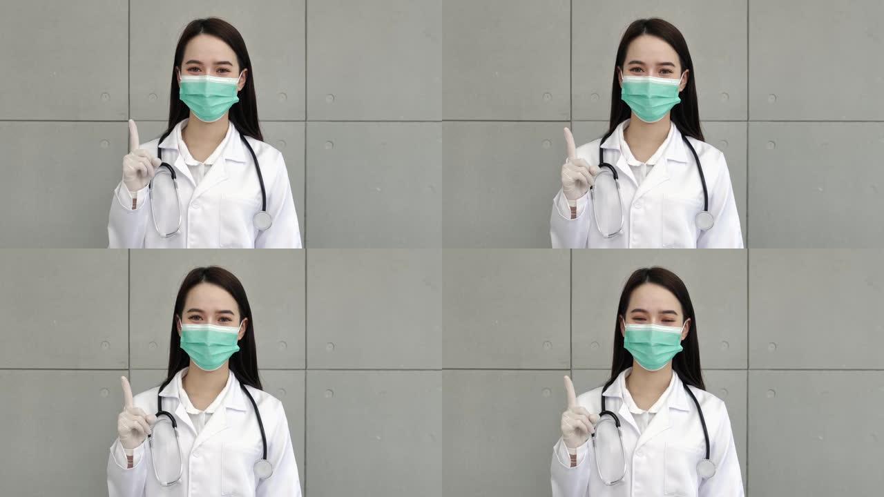 一名亚洲女医生或护士穿着制服，配有听诊器，戴着医用口罩，戴着手套，站着举起右手和食指。