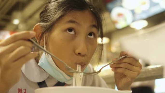 亚洲女学生穿着制服，和哥哥一起在美食广场吃面条汤，生活方式理念。