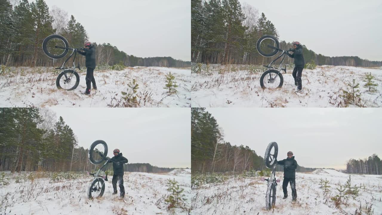 专业极限运动员骑自行车的人在户外举起一辆胖自行车。骑自行车的人留在冬天的雪林里。男子带着戴着头盔和眼