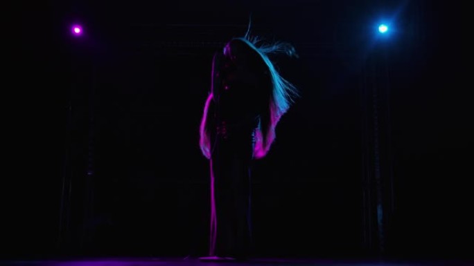 流行歌手在蓝色紫罗兰色灯光照亮的黑暗舞台上表演的仰视图。在现场音乐会上，一头长发飘逸的女人的深色剪影