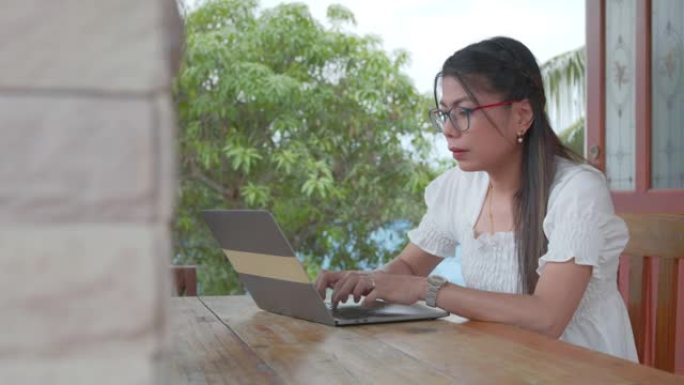年轻的亚洲妇女在前廊在电脑笔记本电脑上打字，并在检疫期间从冠状病毒Covid 19大流行作为新的正常