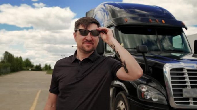 专业卡车司机戴着墨镜，身后停放着带货运拖车的长途半卡车