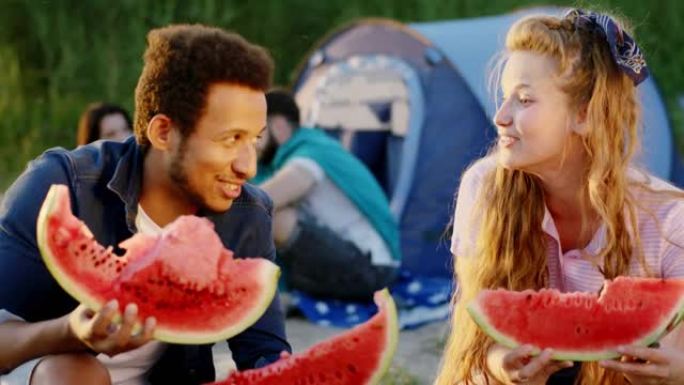 具有超凡魅力的多种族朋友在野餐时聊天，微笑着拿着大块西瓜