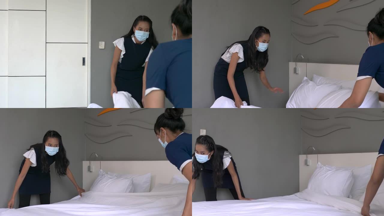 两名戴着医用口罩的年轻女仆在酒店房间的床上换床单