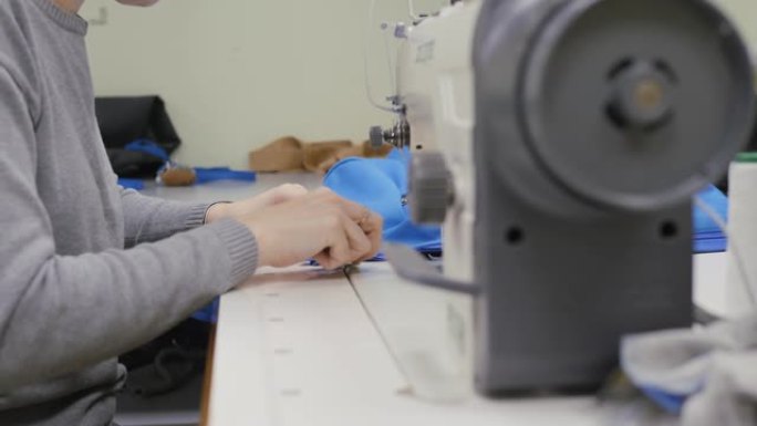 缝纫车间。女人在工业缝纫机上缝纫。双手特写。将拉链插入产品中。