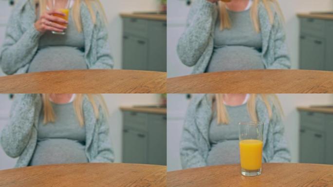 漂亮的孕妇坐在厨房的桌子上做梦，喝着果汁，抚摸着她的大肚子。在家。室内