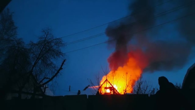 房子的屋顶着火了。居民楼烧毁，村庄。消防员从上方扑灭了起重机上的大火。烟雾和火花。
