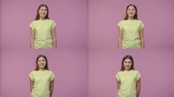 一个自然美模特的肖像撒娇地看着相机，微笑着。穿着黄色t恤长发的年轻女孩在紫色工作室背景上摆姿势。特写