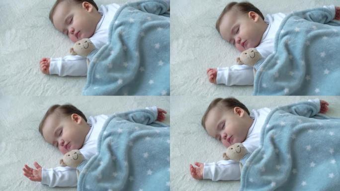 可爱的高加索小婴儿胖乎乎的女婴的真实特写，用泰迪熊睡在舒适的白色和蓝色床上。儿童保育，熟睡的孩子，童