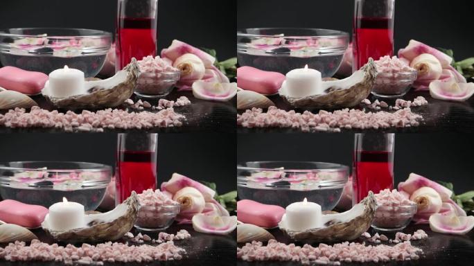 燃烧的蜡烛，香盐，玫瑰精华，玫瑰花瓣，玫瑰肥皂，黑色背景上的贝壳