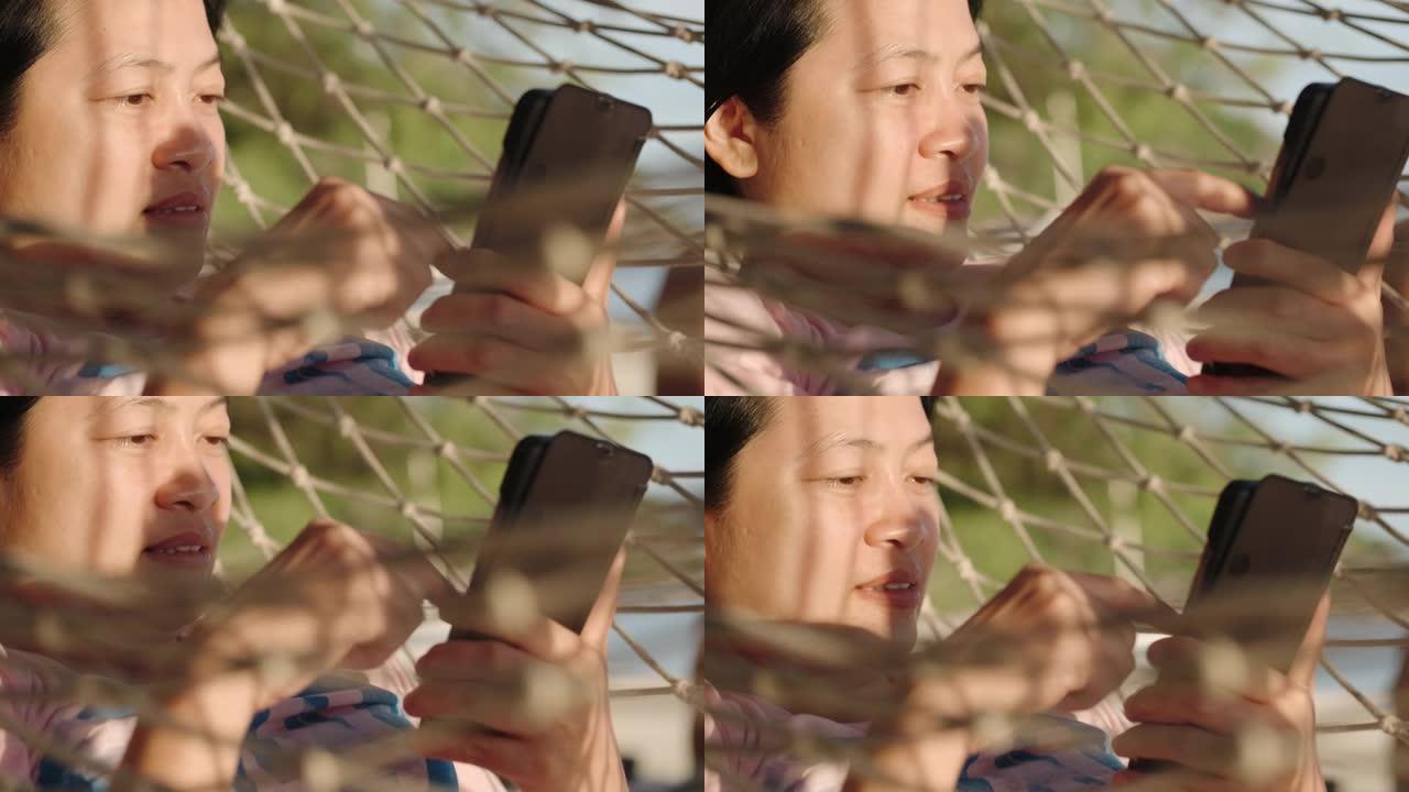 暑假在海滩上使用手机和吊床休息的亚洲妇女的近距离手