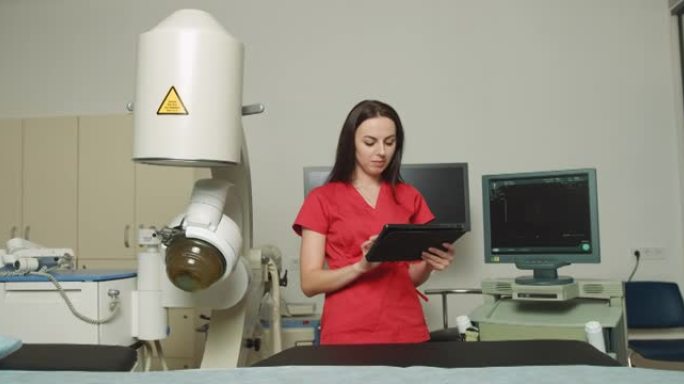 身着红色制服的年轻白人女医生的特写肖像，手持数字平板电脑，在泌尿外科医疗中心现代超声波碎石机附近摆姿