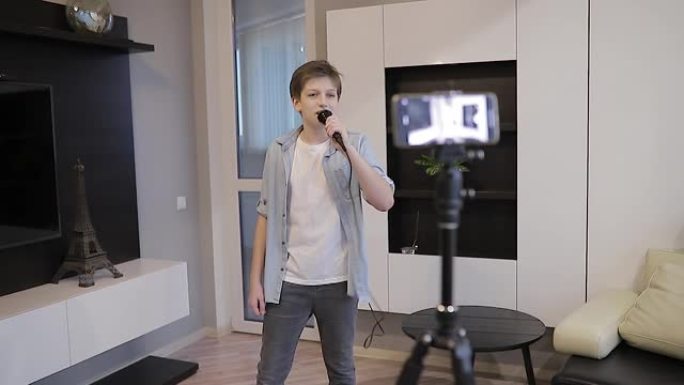 漂亮的青少年博客作者在家里对着麦克风唱歌。看着智能手机与网络摄像头交谈