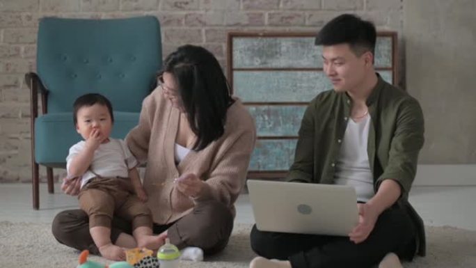 亚洲家庭和小男孩坐在舒适房间的地板上1年。