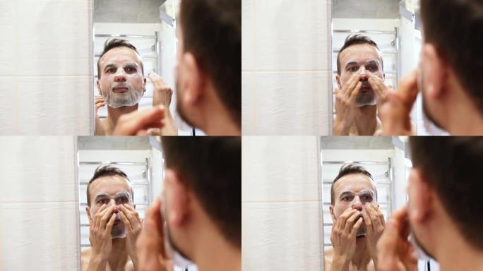 镜子反射微笑千禧一代男人在浴室里涂化妆品面膜。在家进行自我护理、健康和水疗护理。