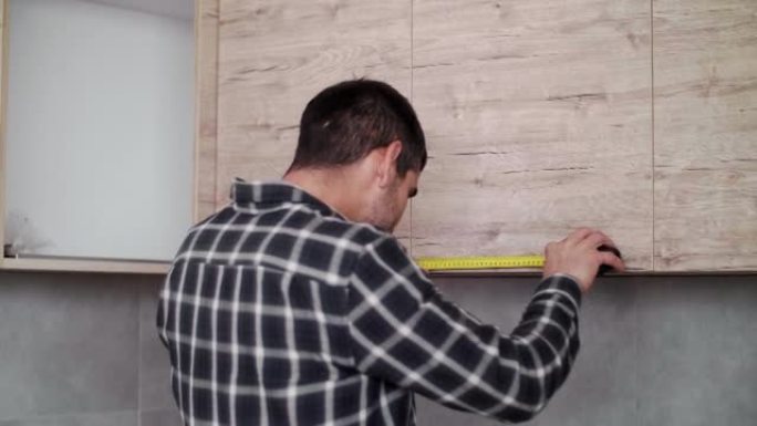 木匠用仪表测量新厨房的一部分架子。
