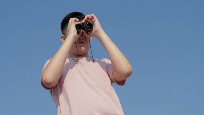 亚洲男孩用双筒望远镜看着山顶上的蓝天，生活方式的概念。